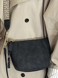 Black matte shell bag with wide geometric strap and gold hardware on beige trench coat