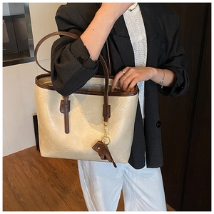 Detail view of large beige tote bag with brown straps and bird pendant accessory