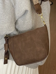 Brown suede shell crossbody bag with a wide jacquard wave strap and gold hardware