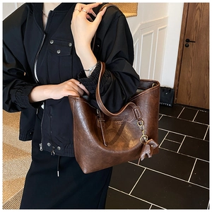 Detail of vintage brown tote bag with leather leaf charm and embossed logo on texture