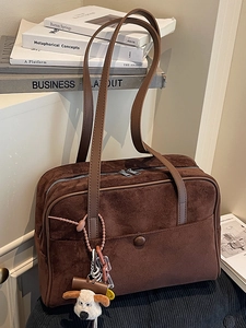 Vintage dark brown suede bowling bag with dual straps and cute dog charm on a soft chair