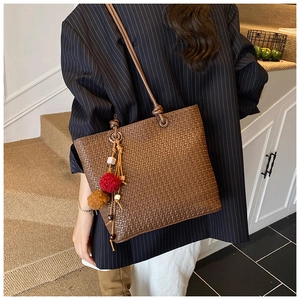 Close-up of woven brown leather tote bag with decorative red and brown plush pom-pom charms