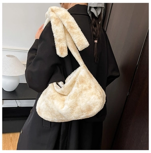 Detail of soft cream plush bucket bag with wide shoulder strap worn over black coat