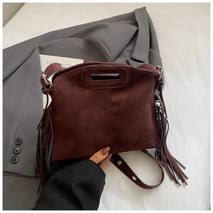 Detail of burgundy suede crossbody bag with fringe accents and hollow handle on suit