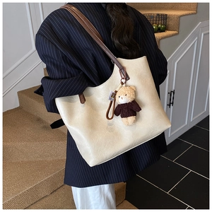 Detail of cream tote bag with bear charm on a navy blazer showing the smooth faux leather texture