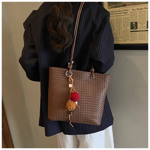 Close-up of brown woven tote bag with colorful pom-pom charms on office style outfit