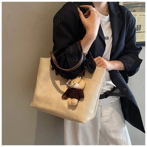Detail view of large cream tote bag with contrast brown straps and plush bear charm
