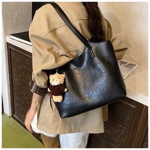 Close-up of black leather tote bag with brand logo and cute plush bear charm detail