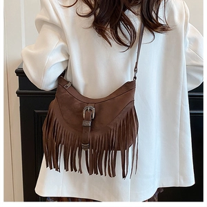 Detail of brown suede crossbody bag with long tassels and vintage metal buckle on strap