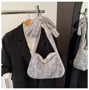 Detail of grey plush shoulder bag featuring a large decorative bow and gold metal clasp