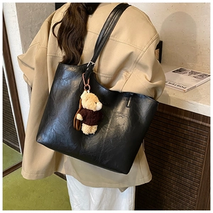 Detail of black tote bag with wrinkled texture, adjustable strap and cute plush bear charm