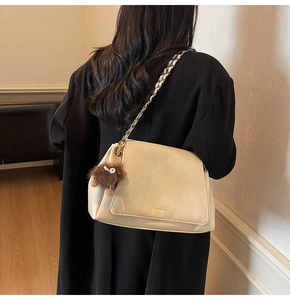 Detail of beige shoulder bag with chain strap and a brown plush monster charm accent