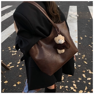 Detail of a large brown tote bag with leather texture and cute bear charm in street setting