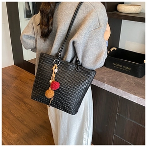 Detail of black woven tote bag with shoulder strap and stylish pompom charm for women