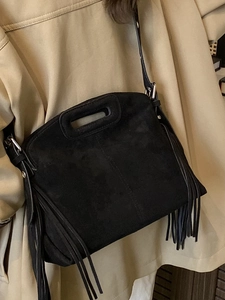 Black faux suede tote bag with fringe details and adjustable shoulder strap worn by model