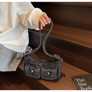 Detail of black washed denim underarm bag featuring utility pockets and silver metal buckles