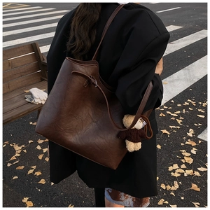 Close-up of a large dark brown tote bag with fuzzy bear charm on a street background