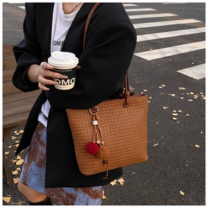 Close-up of woven texture on a brown tote bag with colorful plush ball charms and accessories