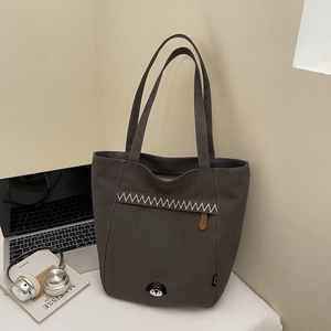Détail d'un sac cabas en toile grise avec surpiqûres ondulées et broderie petit chien