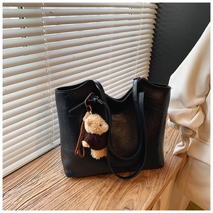 Close-up of black textured leather tote bag with a cute brown teddy bear plush charm