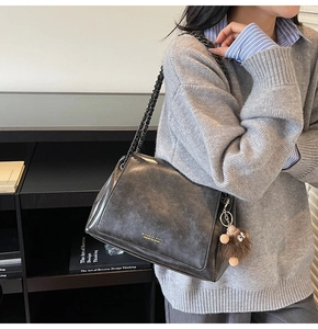Detail of dark grey leather tote bag with black chain strap and plush mascot charm
