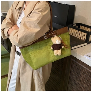 Detail of green suede tote bag with brown leather handles and a cute bear charm accessory