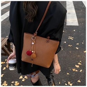 Detail of brown woven tote bag with plush tassel charm in a cozy autumn street setting