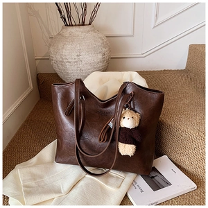 Detail view of large dark brown patent leather tote bag with ZSKE & BAG logo and teddy bear charm
