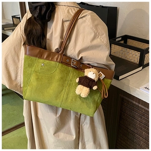 Detail of green suede tote bag featuring brown leather trim and cute bear charm pendant