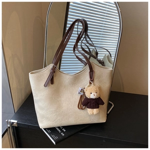 Close-up of cream leather tote bag with brown straps and a cute brown plush bear charm