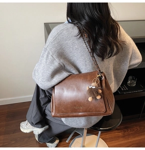 Detail of a brown leather tote bag featuring a chain strap and a cute furry eye charm