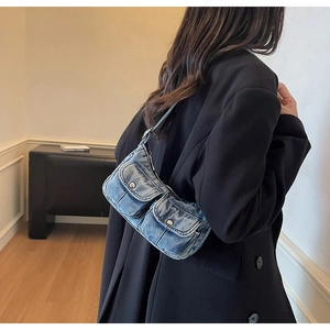 Detail of blue denim motorcycle shoulder bag with silver buckles worn with black suit