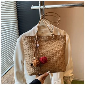 Detail of khaki woven tote bag showing fine texture and stylish bicolored pompom charms