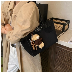Detail of black canvas tote bag with leather strap and cute brown plush bear pendant