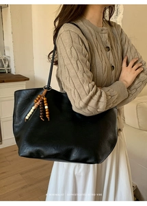 Detail of a large black faux leather tote bag featuring a decorative wooden bead charm