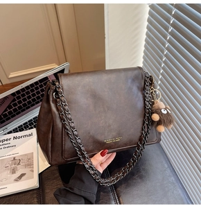 Detail view of brown vintage leather tote with metal chain strap and cute monster charm