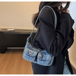 Detail of blue denim shoulder bag featuring dual front flap pockets and metal button accents