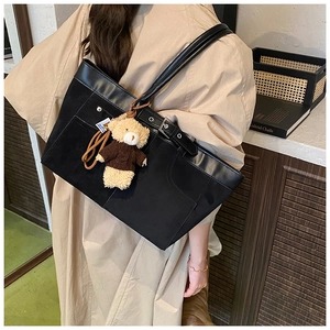 Detail of black tote bag with leather straps and a cute brown plush bear charm