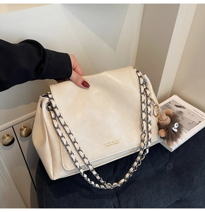 Close-up of beige leather shoulder bag with gold chain strap and plush monster charm