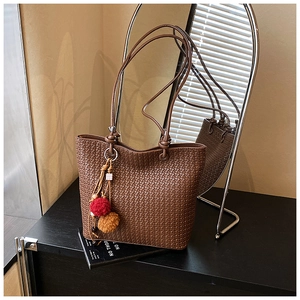 Detailed view of brown woven tote bag with colorful pompom charm on a magazine