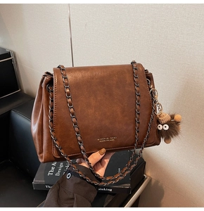 Detail of dark brown matte leather tote with chain strap and plush monster charm