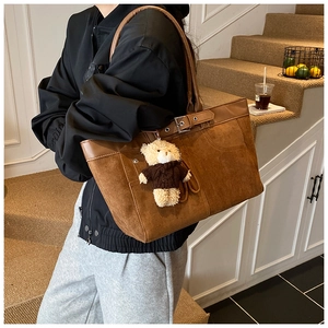 Detail of a brown suede tote bag with metal buckle and a cute teddy bear charm