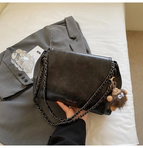Close-up of black matte leather tote bag with metal chain strap and cute monkey charm