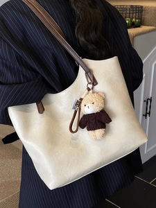 Large cream leather tote bag with brown straps and cute bear charm for daily commute