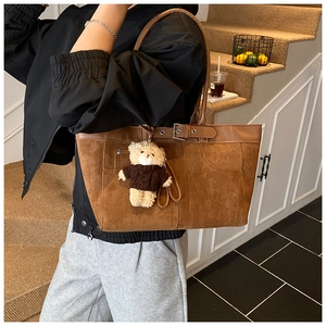 Brown suede tote bag detail featuring visible stitching and a cute plush bear charm