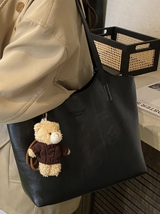 Large black leather tote bag with bear charm shown on model for autumn fashion