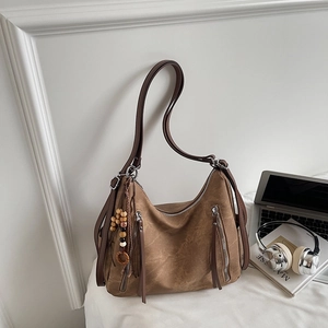 Close-up of brown suede hobo bag featuring decorative zippers and tassel bag charm