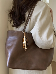 Vintage brown leather tote bag with wooden bead tassel shown on a beige trench coat