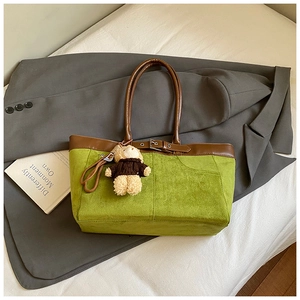 Top view of a green suede tote bag with brown leather accents and a plush bear charm