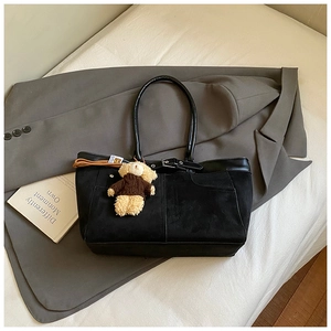 Detail of black tote bag with matte texture, leather trim and cute bear charm accent